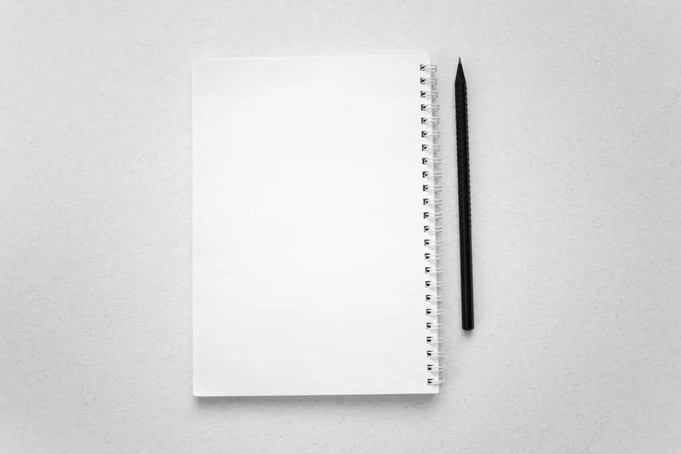 Foto ilustrasi notebook spiral kosong dan alat tulis pada meja putih